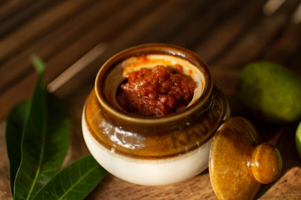 Traditional Indian mango pickle in a rustic ceramic jar on a wooden surface, perfect for food lovers.